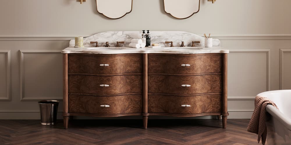 Wooden vanity with marble countertop, twin brass faucets, and two decorative mirrors above. In a classic bathroom setting, adorned with wall sconces, small accessories, and a neatly folded towel.