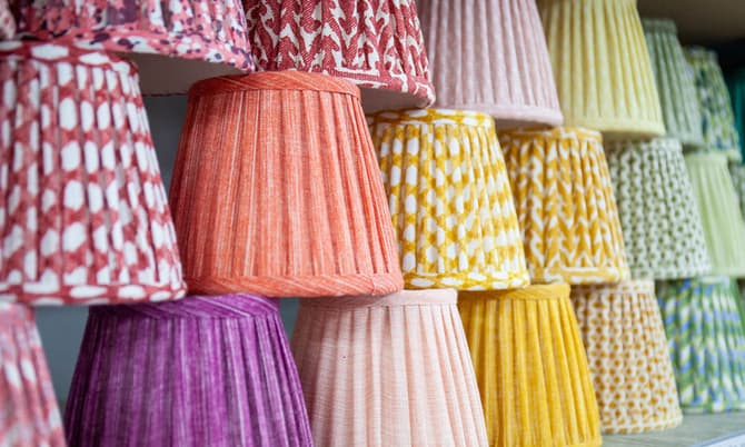 Lampshades with diverse, vibrant patterns and colors are displayed on shelves, neatly stacked and arranged in rows by color, creating a visually striking and organized presentation.
