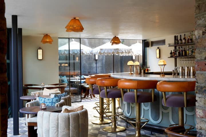 A stylish bar area with leather bar stools surrounding a counter, pendant lights above, and a view of an outdoor patio with umbrellas through glass doors.