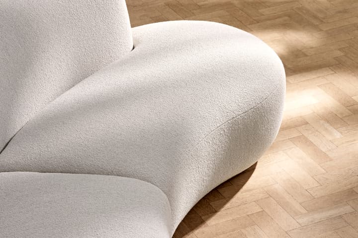 A curved, cream-colored couch sits on a wooden parquet floor, catching soft sunlight.