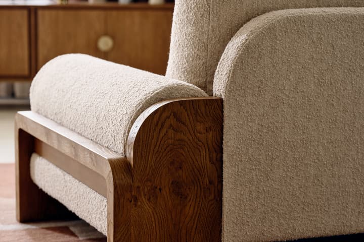 The white, textured armchair with wooden legs sits on a patterned rug, adjacent to a wooden sideboard adorned with decorative vases, a bust, and a plant.