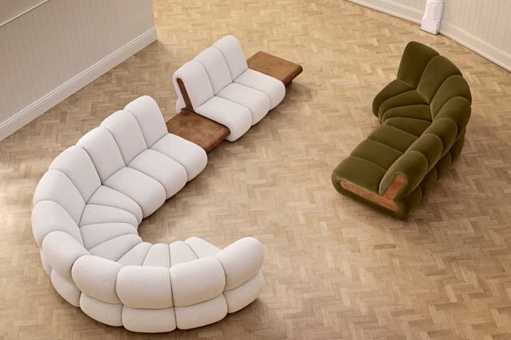Curved white and green sofas with wooden inserts, arranged on a herringbone-patterned wood floor by a white-paneled wall with molding and a visible support column.