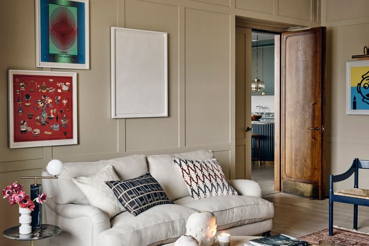 A beige living room (context) features a light gray sofa adorned with patterned pillows (object), a side table with flowers, and framed artwork on the wall (action), adjacent to a partially open wooden door revealing a kitchen. Text: "I MISS WHAT I'VE NEV