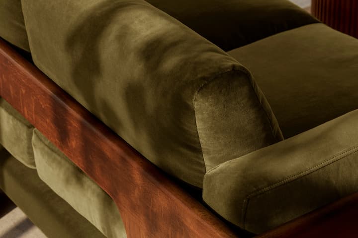 A green cushioned sofa with a wooden frame sits indoors on a light-colored tiled floor, adjacent to a wooden coffee table with a marble top.