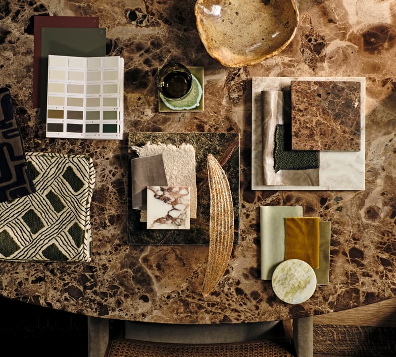 Various fabric swatches, color palettes, tiles, and a decorative dish rest on a marble tabletop, arranged for an interior design project.