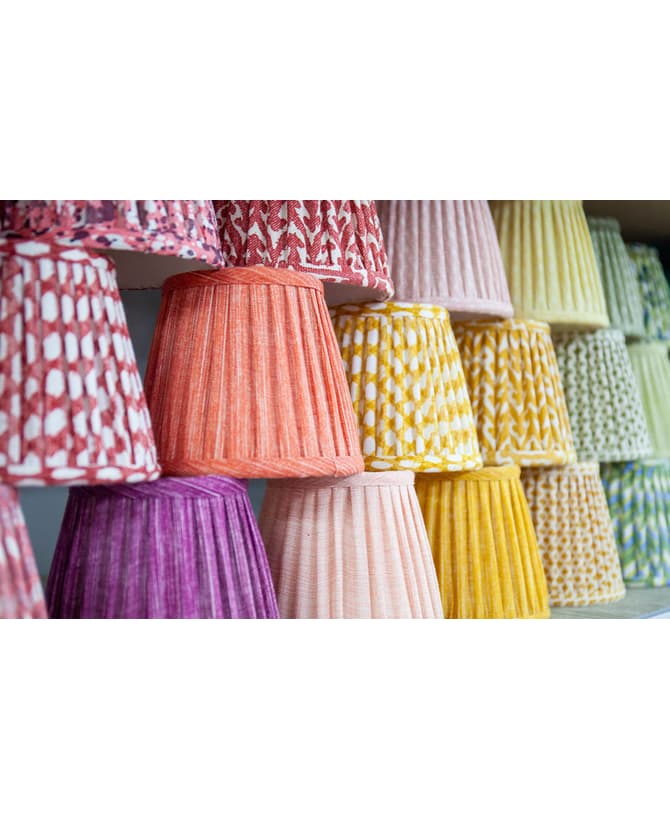 Lampshades with diverse, vibrant patterns and colors are displayed on shelves, neatly stacked and arranged in rows by color, creating a visually striking and organized presentation.