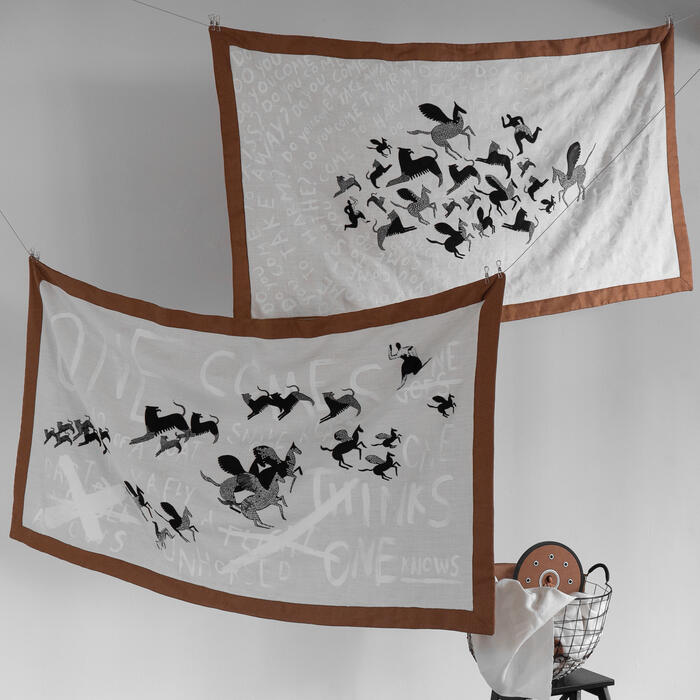 Two white cloths with brown borders featuring various animal silhouettes hang on a line against a plain backdrop. Texts: "ONCE SOMEONE SAID, DO YOU KNOW?" and "SEVERAL PEOPLE THINKS ONE KNOWS". A basket holds a folded cloth and round objects.