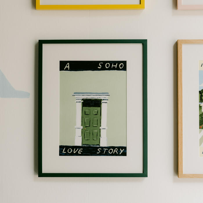 Three framed paintings on a wall. The top left painting shows a drink and lemon with the text "FOR A PICANTE." The bottom middle painting depicts a green door with “A SOHO LOVE STORY” written.