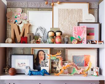 A collection of decorative items is displayed on two ornate shelves, including art pieces, toys, figurines, a dragon sculpture, and a clock. One image reads, "ANY IDIOT CAN FACE A CRISIS. IT’S THIS DAY-TO-DAY LIVING THAT WEARS YOU OUT." Another sign reads