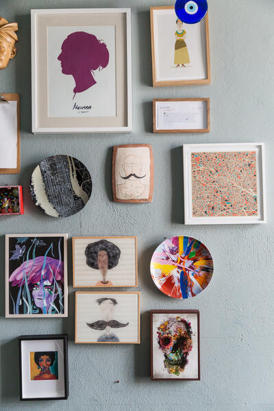 Framed and unframed artworks are arranged on a light blue wall, featuring various colorful abstract, portrait, and patterned designs, and including a framed silhouette labeled "Melissa is Perfect."