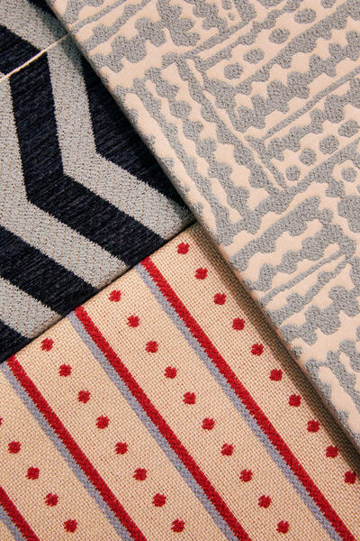 Three patterned fabric samples overlapping; one with blue and white chevron design, another with blue abstract waves on beige, and the third with red polka dots and stripes on beige.