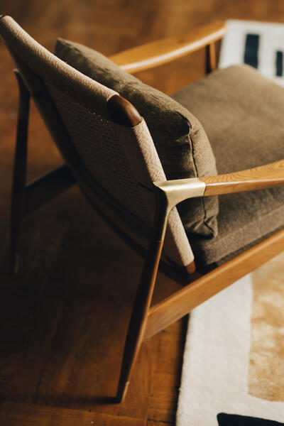 A wooden armchair with woven rattan backrest and cushioned seat, positioned on a wooden floor beside a partially visible rug.