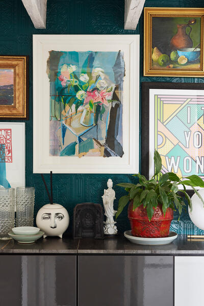 Collection of framed art and a mirror hung on a teal textured wall above a cabinet; items include a plant in a red pot, a face pot, and glassware. Text: "I THINK YOU ARE WONDERFUL".