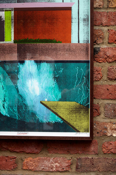 A framed abstract artwork hangs on a brick wall, featuring layered rectangular color blocks with green plants and a blue watery effect. The text reads "Hackney Cool" and an unreadable signature.