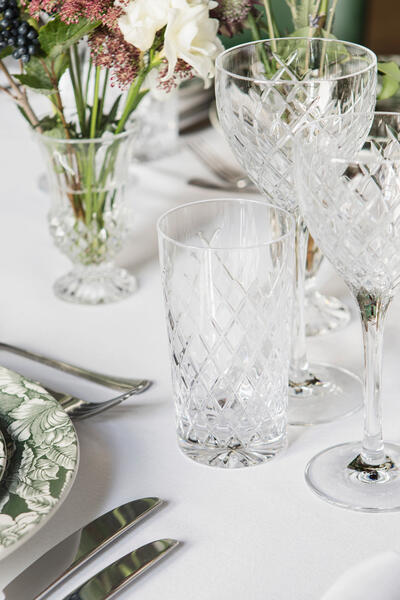 Two floral-patterned plates, crystal glasses, cutlery, and flower arrangements set neatly on a white tablecloth.