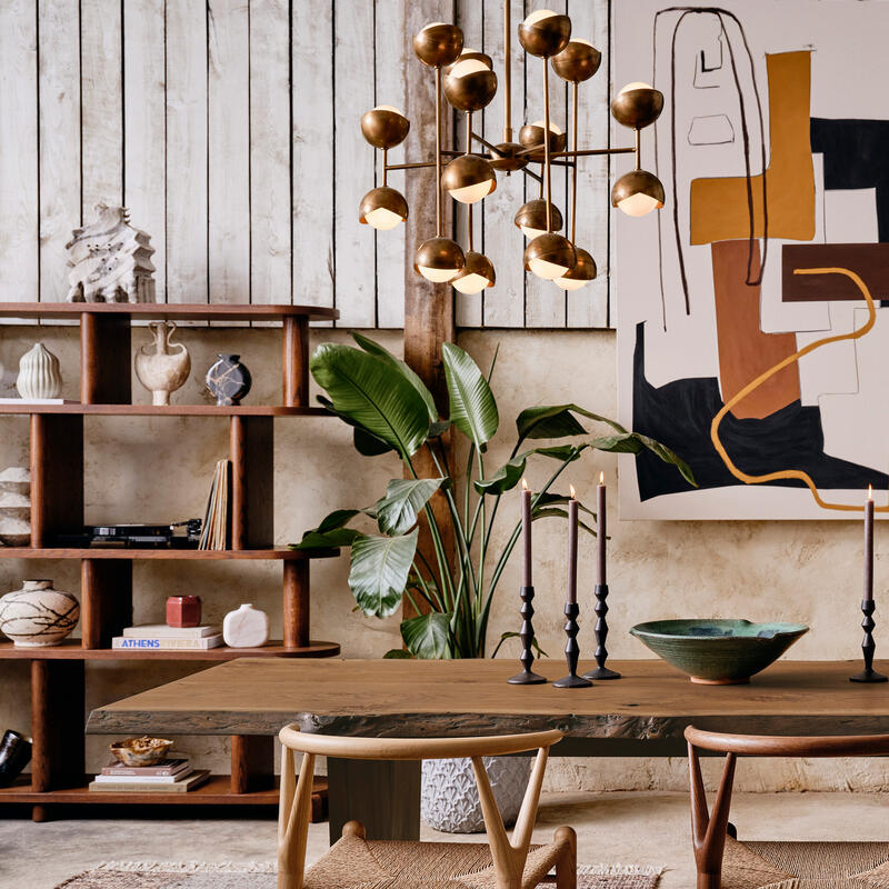 A wooden dining table with chairs is adorned with candlesticks and a bowl. The environment features a modern chandelier, a potted plant, a bookshelf with decorative items, and abstract art.