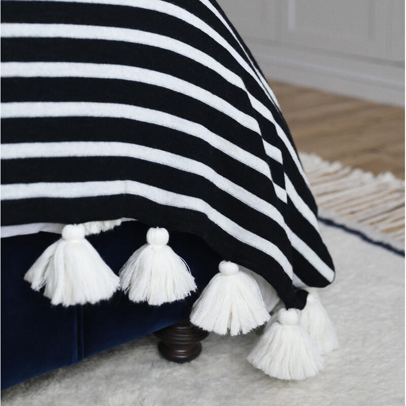 A black and white striped blanket with white tassels draped over a dark blue upholstered bed in a room with hardwood floors and light-colored walls.